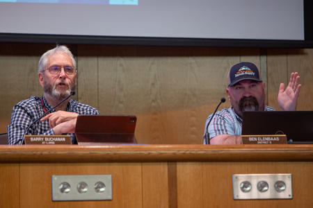 Two County Council members sit behind a wooden desk during a meeting. 