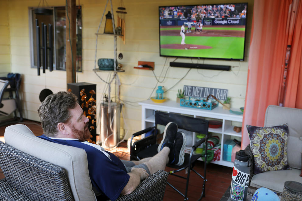 A man sits in a chair watching a baseball game on tv