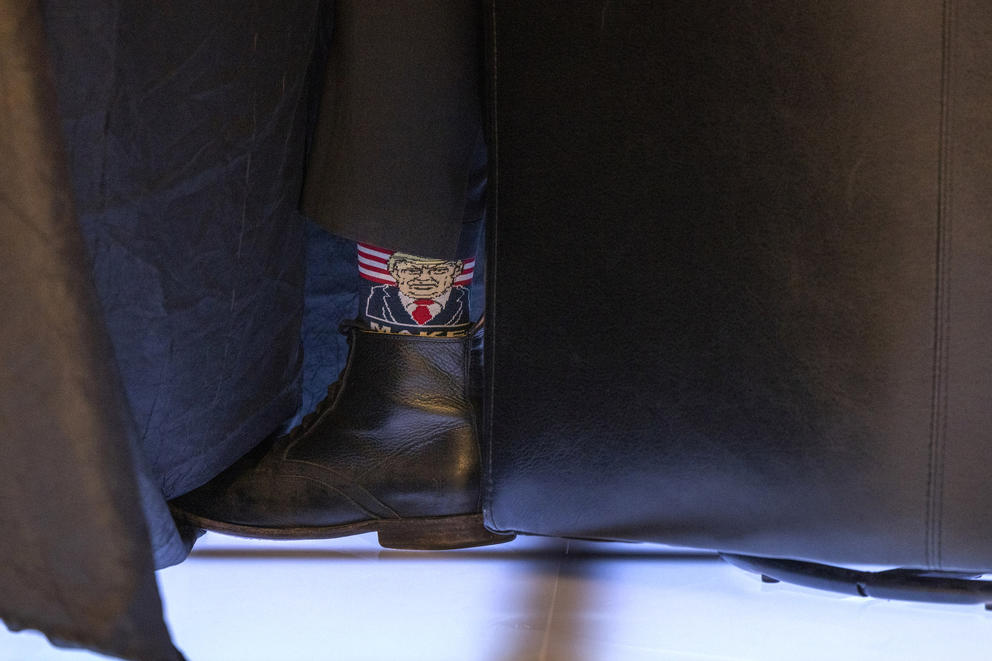 A shoe is visible under a table, a sock peeks out with Donald Trump's likeness on it