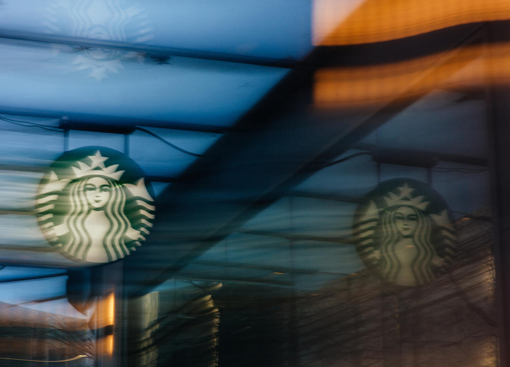 A ghostly green Starbucks sign is reflected against a window in blue evening light.
