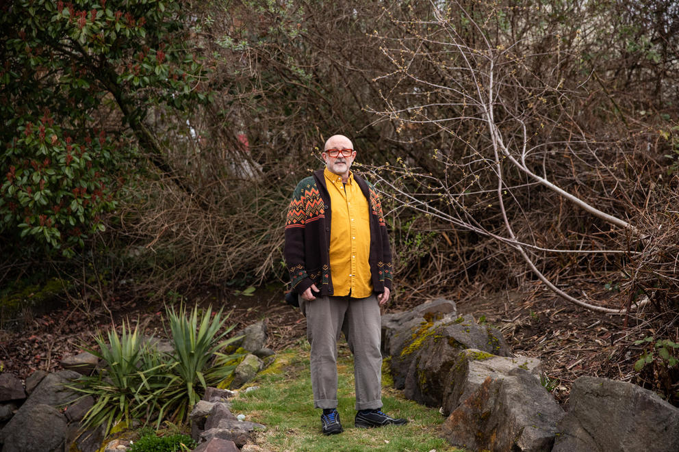 Roger Kelley stands in an overgrown lot surrounded by branches and vines