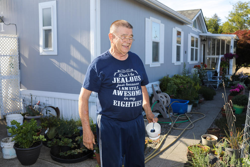 A man wearing a blue shirt stands outside his home in the sun