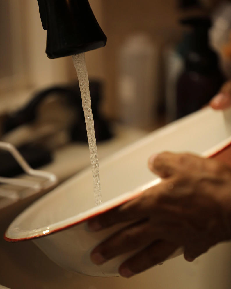 A close up of hands on a bowl filling up with water from a kitchen sink