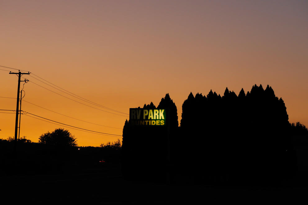 The sun sets over silhouetted trees and a sign for Sun Tides RV Park
