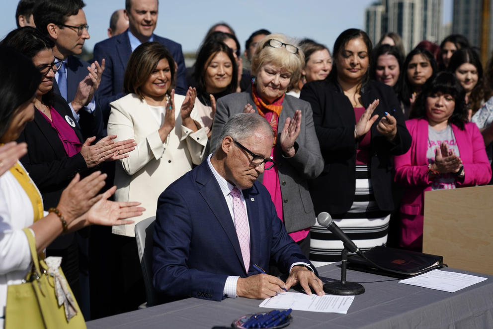 Lawmakers, including primary bill sponsor state Sen. Karen Keiser clap as Washington Gov. Jay Inslee signs bill to protect abortion pill access