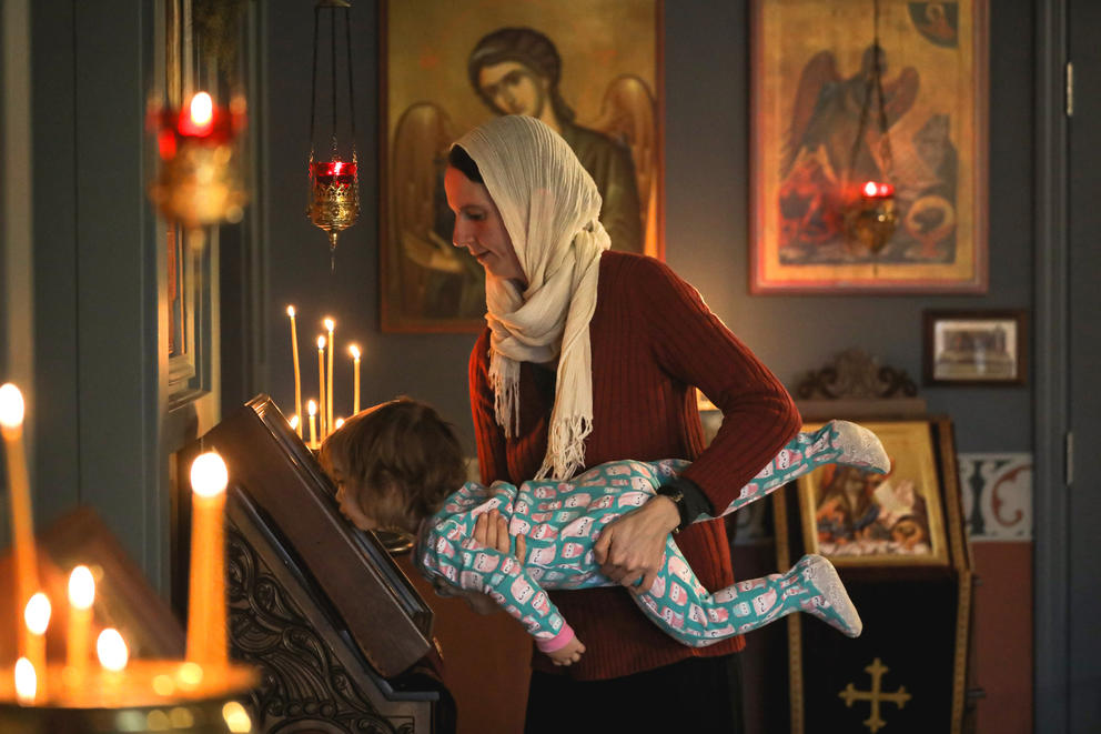 A woman holds a child up to kiss an icon inside a church