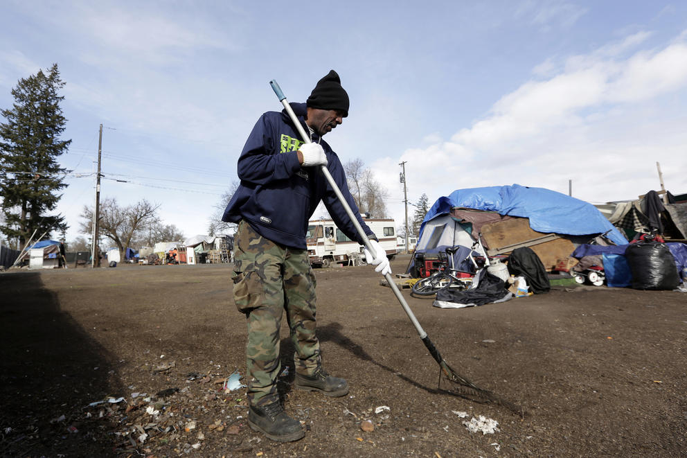 A man rakes up trash in a homeless encampment
