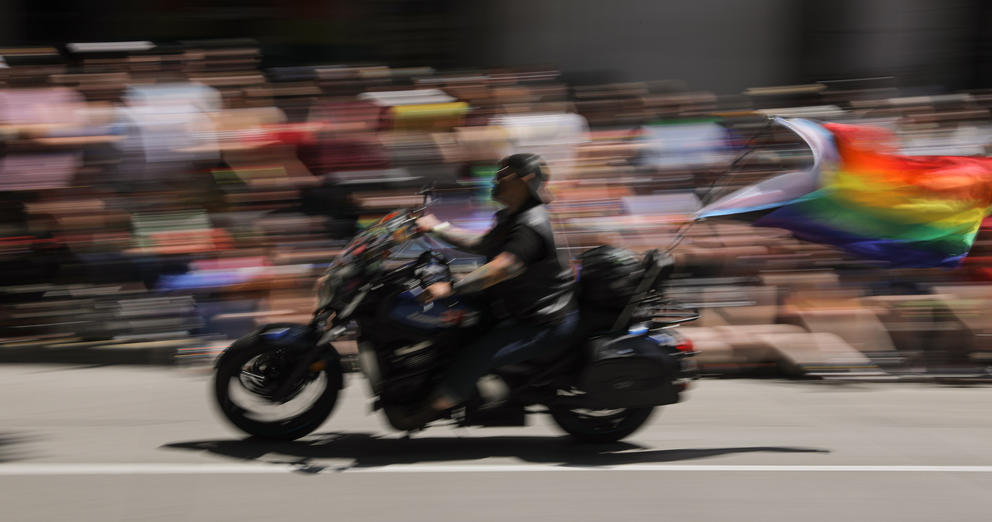 A motion blurred image of a motorcycle rider carrying a Pride flag