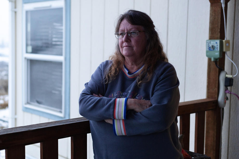 A woman poses in front of her patio in Moxie Community. Her sweatshirt is a gray-ish blue color, with colorful, striped cuffs.