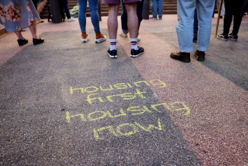 sidewalk chalk at a rally reads housing first, housing now