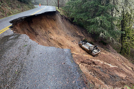 a car lies in a crater created by a landslide on a rural road.