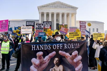 A crowd of pro-abortion protesters. One man in the front holds a banner reading "Hands off Roe!!!"