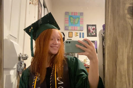 A young woman in a graduation gown takes a mirror selfie