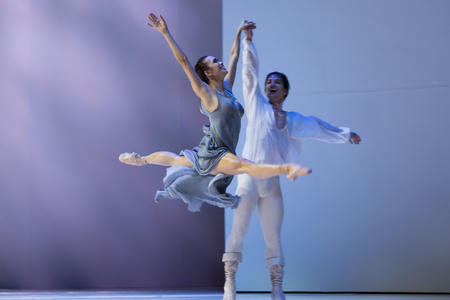 two ballet dancers performing on stage, the woman leaping in the splits, man supporting