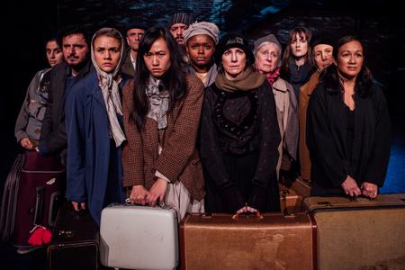 a group of actors dressed as immigrants with suitcases