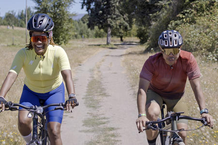 bipoc woman and man riding a bicycle on a gravel path