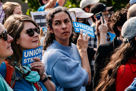 a crowd of people protesting with a close up of a woman in a blue sweater in the center
