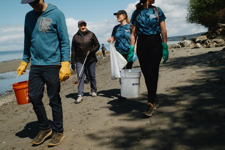 four people walk on a beach holding bags and buckets