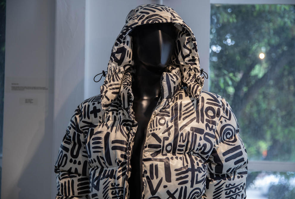 A mannequin wears a shiny, puffy white jacket covered with abstract black paintbrush symbols