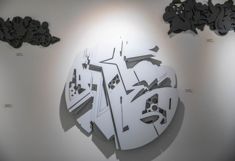 Two black and one white angular, graffiti-inspired three-dimensional shapes hang on the wall
