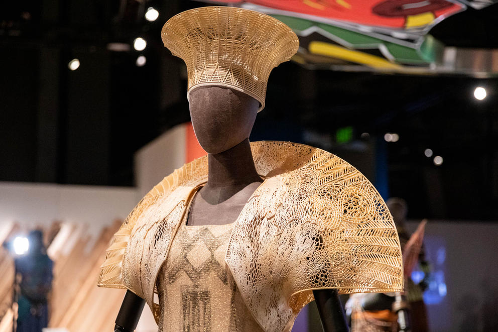 A beige, intricate headdress and collar is worn by a mannequin and appears lace-like