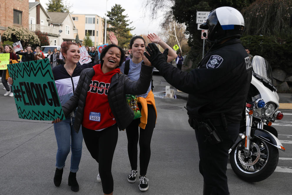 Students give an SPD officer a high-five while marching from Roosevelt High School to University of Washington's Red Square 