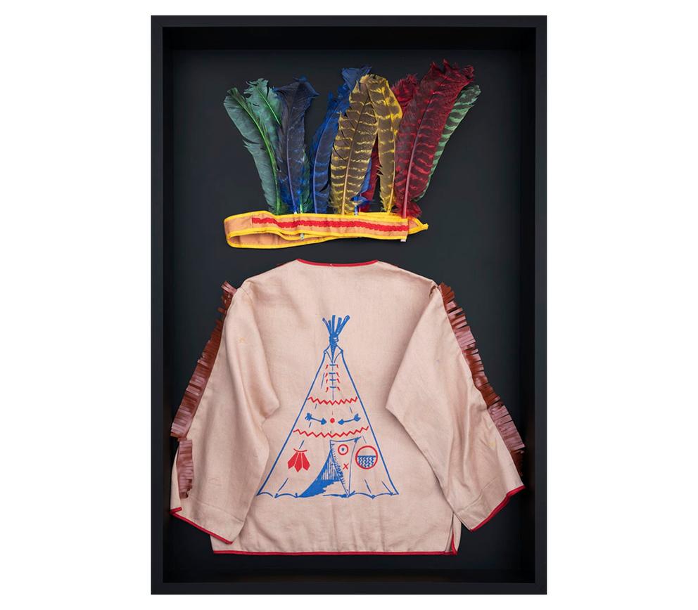 Tan shirt photographed on black background, with a colorful fake-feather headdress up top