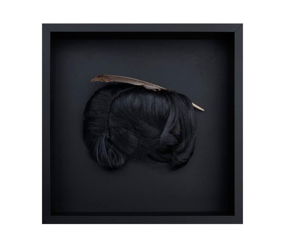 Black wig with feather on a black backdrop