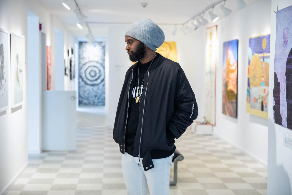 a man in a black jacket and grey beanie hat stands in the middle of an art museum