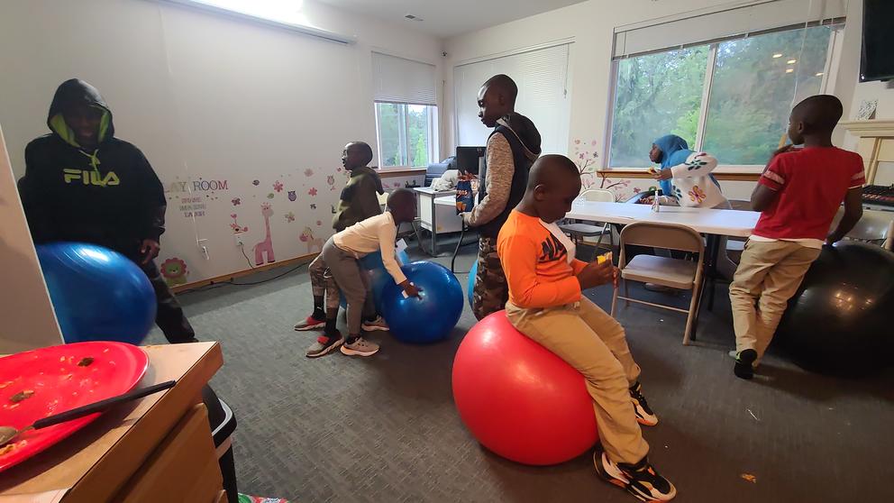 Children sit and bounce on red and blue inflatable yoga balls in a play room. 