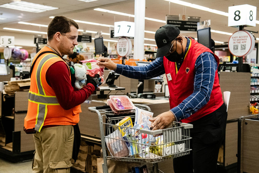 A grocery manager at right hands items to a clerk at checkout.