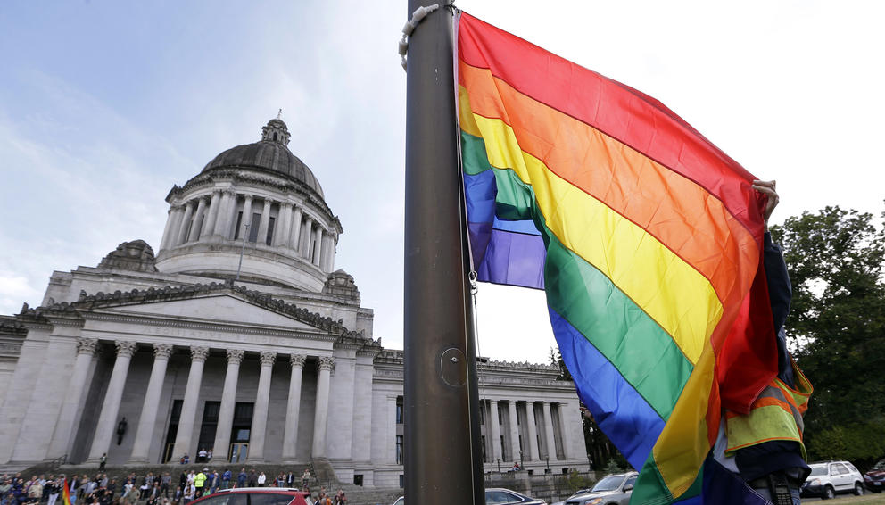 A state worker unfurls a rainbow flag in front of the Washington state Capitol 