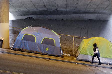 Tents line a sidewalk under a freeway overpass