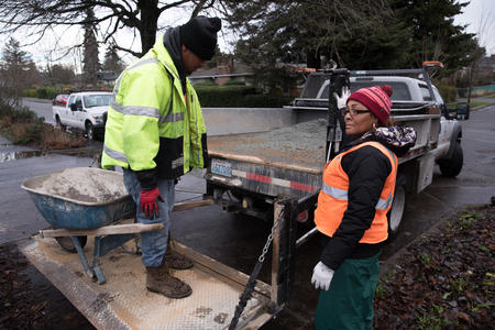 Seattle Conservation Corps crew member Chris Townsell (left) is lowered on a truck lift with a wheel barrow by crew member April Winfrey (right) at Angel Morgan P-Patch Community Gardens in Seattle's Rainier Valley