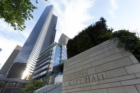 the exterior of seattle city hall with a skyscraper in the background and a blue sky above