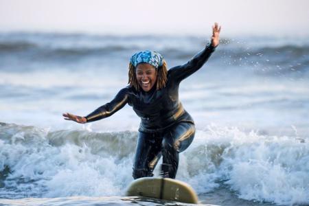 Black woman standing on surf board riding wave near shore