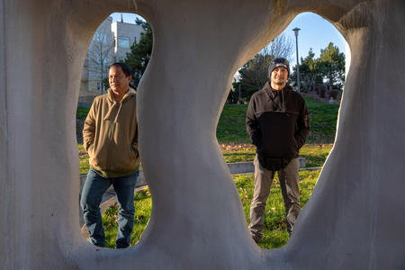 Workers Mickel Mendez and Norberto Cabrela stand framed by public art in a Seattle park